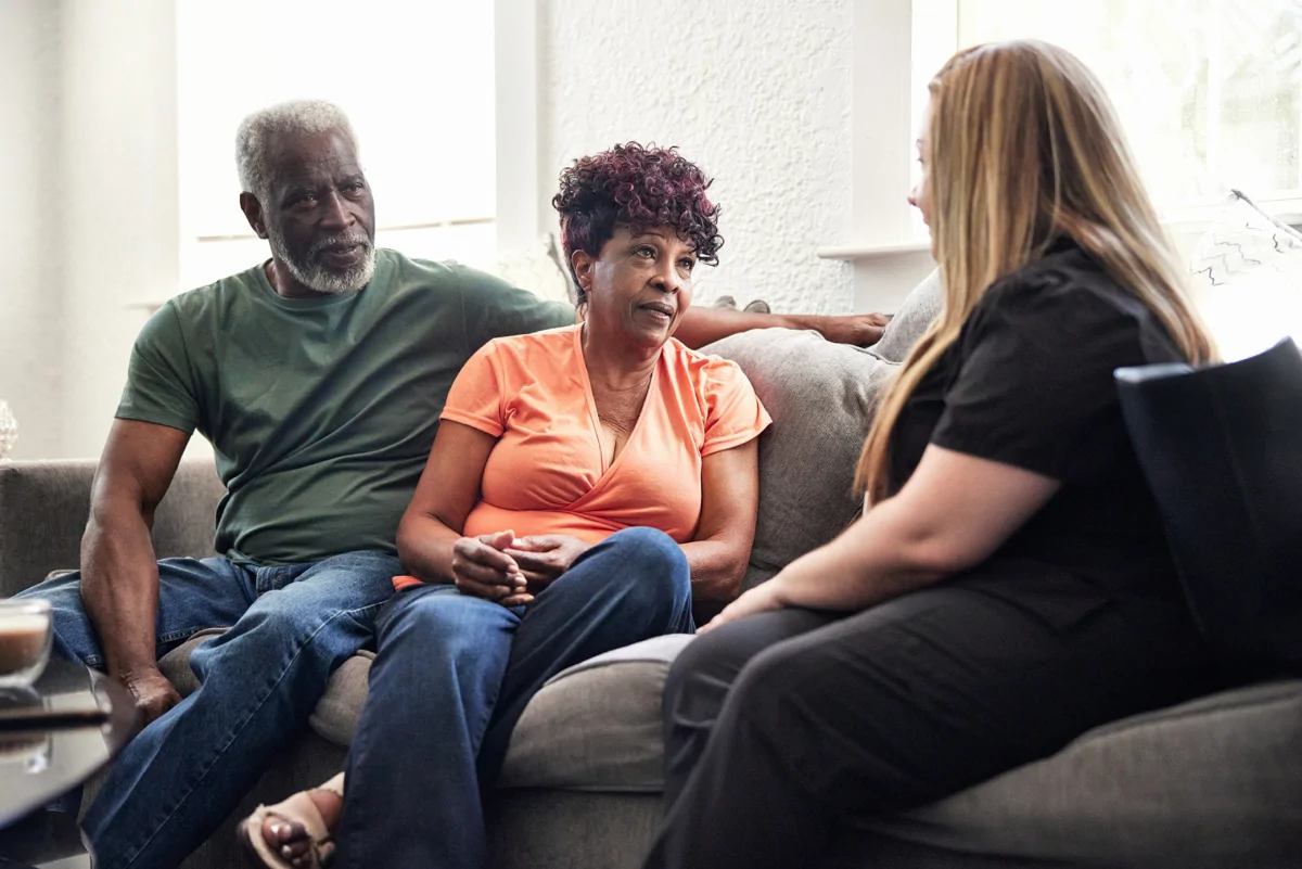 Image shows three people sat on sofa talking