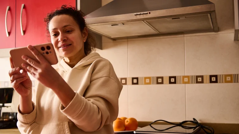 Woman standing in her kitchen looking at her phone