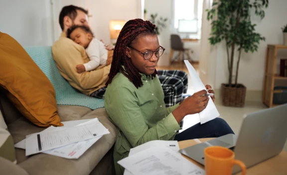 Casually clothed woman working from home while her husband is holding their sleeping baby