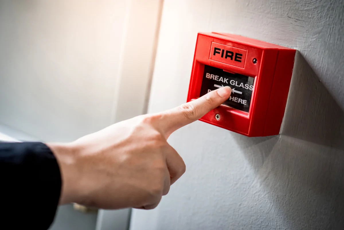 Image shows a person pressing a red fire alarm
