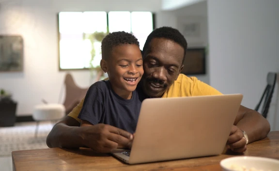Dad and son sitting at table looking at a laptop