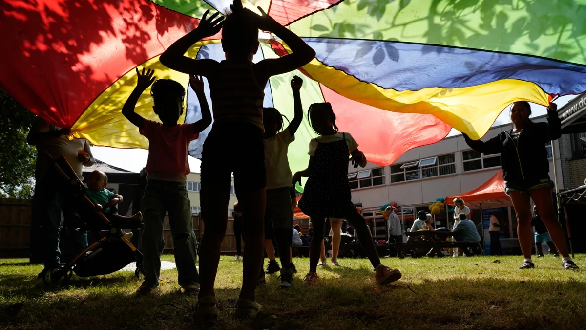 Children playing underneath a colourful parachute at Pollards Hill Wellbeing Studio launch event