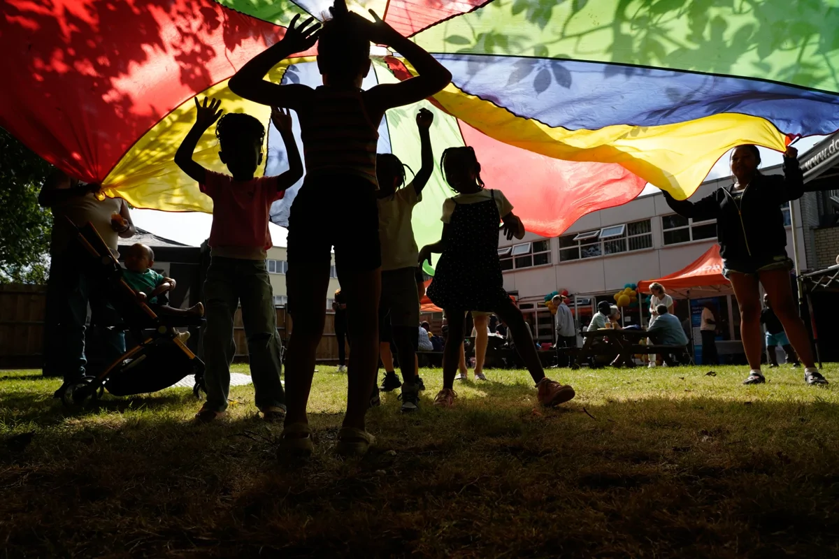 Children playing underneath a colourful parachute at Pollards Hill Wellbeing Studio launch event